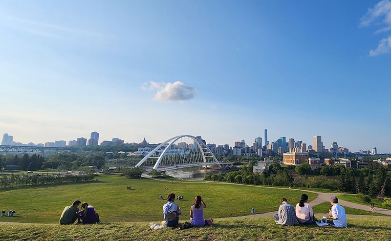 people sitting on graasy hill overlooking the Walterdale bridge and downtown Edmonton