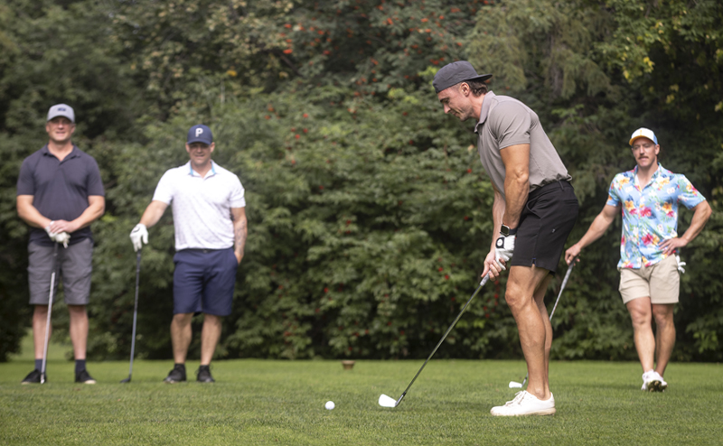 A person lining up their golf swing while three other people wait in the background.