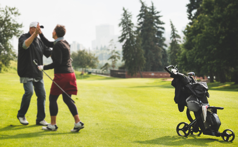 People high-fiving on a golf course near a pull cart
