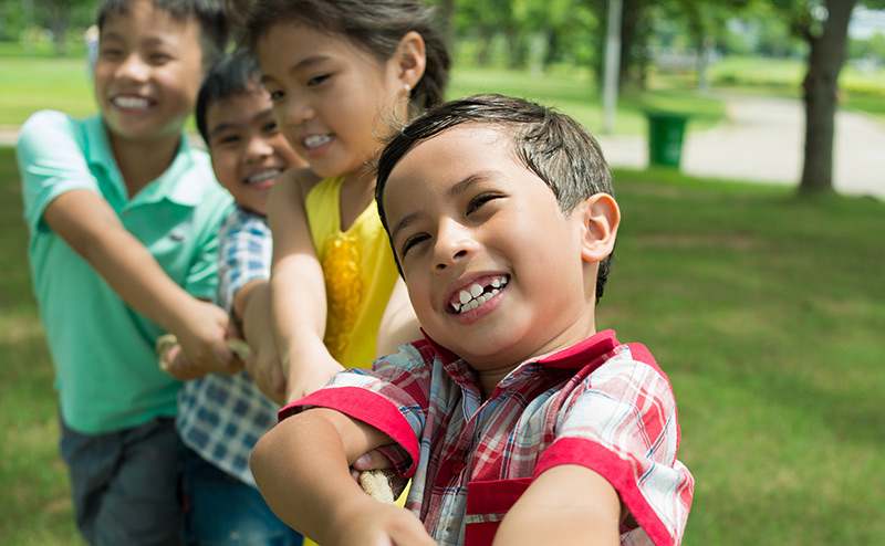 four children playing tug-o-war in park