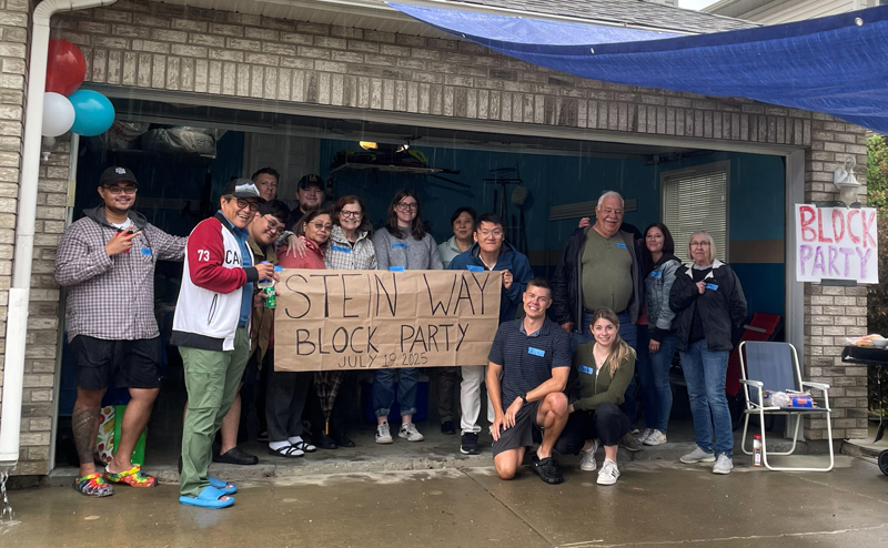 A group of people in a garage holding a block party sign