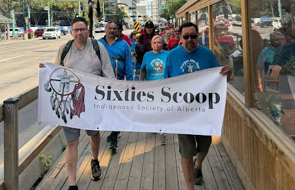 group of people walking with sixties scoop banner