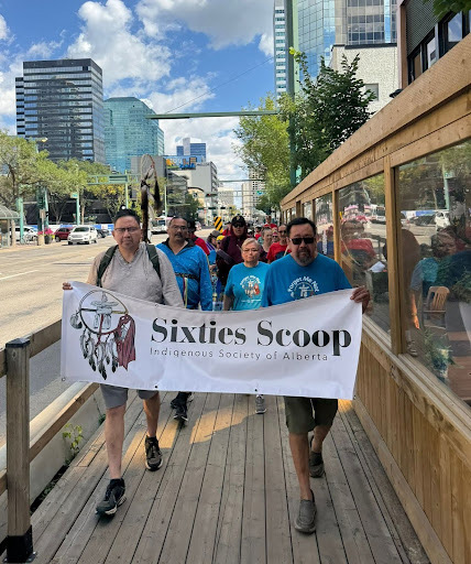 indigenous persons walking with sixties scoop flag