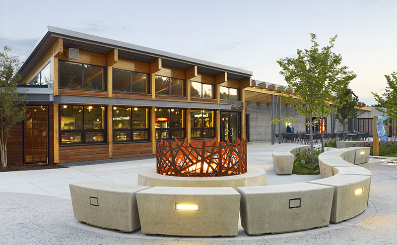 A section of the Edmonton Valley Zoo main entrance plaza, which features trees, benches, decorative lighting and the Wild Neighbours Cafe entrance.