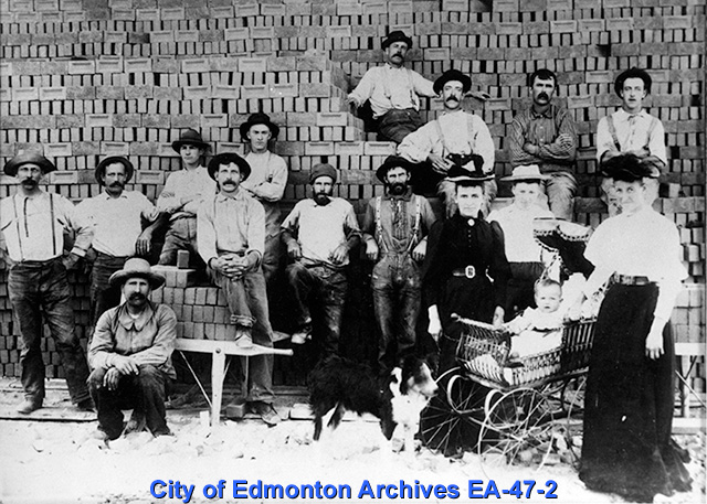 A group of workers standing before a large stack of bricks.