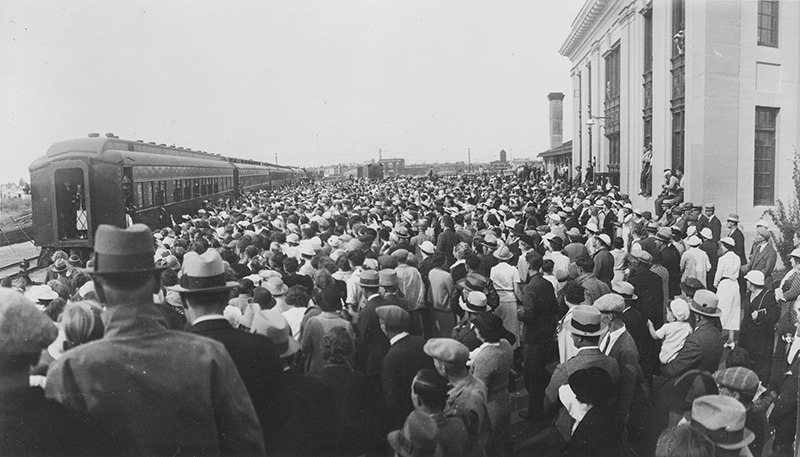Black and white photo of a large crowd standing near a train.