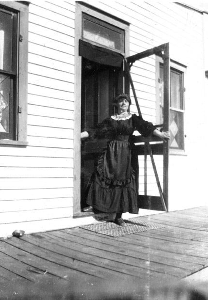 A woman standing at the doorway of a farmhouse.