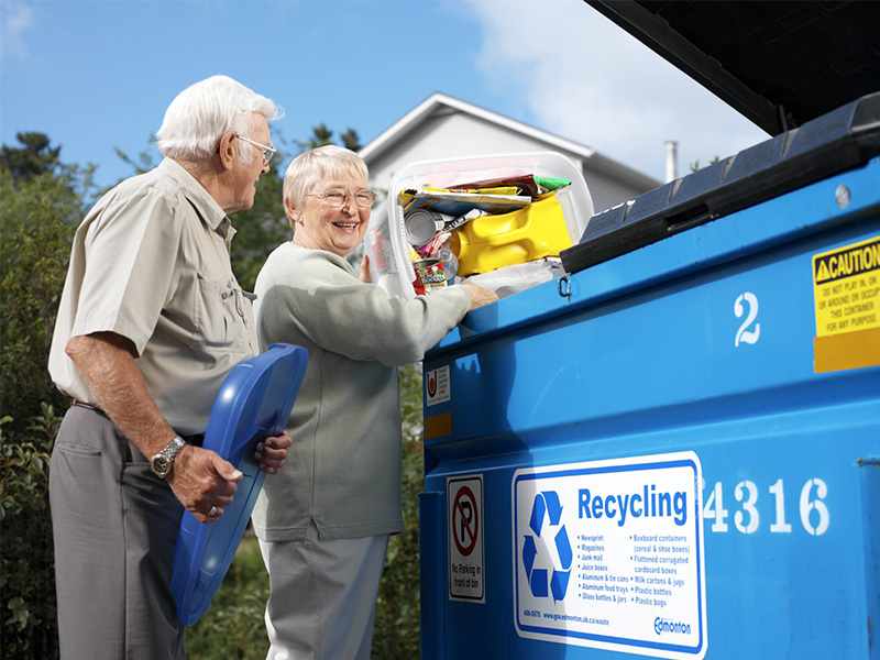 An elderly couple placing their recyclables in an apartment blue bin.