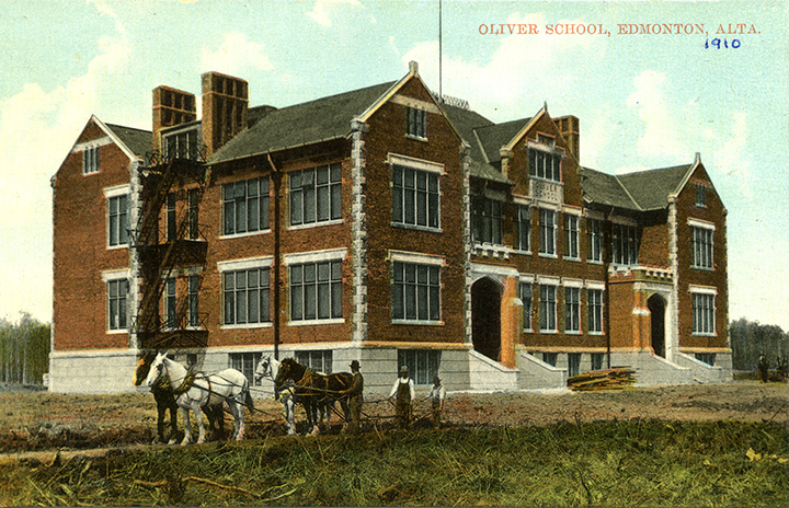 Colourized photo. A brown multi-story school building. Three people stand outside of the building, next to four horses that are tied together. The building has two entrances in front, each with a stairway. Another scaffold-style stairway is visible on the left side of the building, with landings at each floor. Text overlaid in the top-right corner reads "Oliver School, Edmonton Alta." below that text, "1910" is written in blue pen.