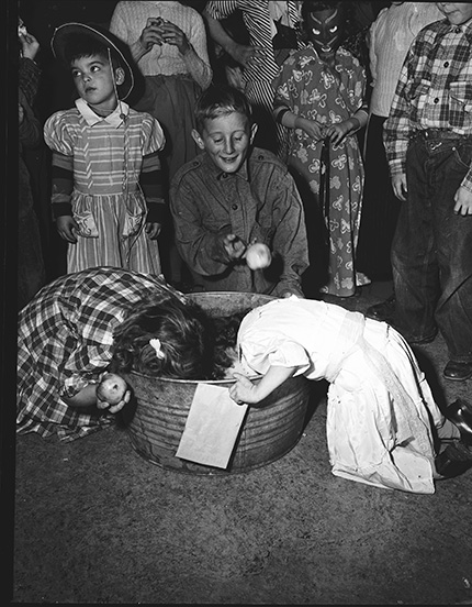 Children dressed in costumes, bobbing for apples