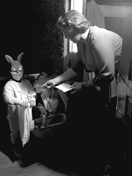 Trick-or-treating child in a rabbit costume being handed candy by a woman.