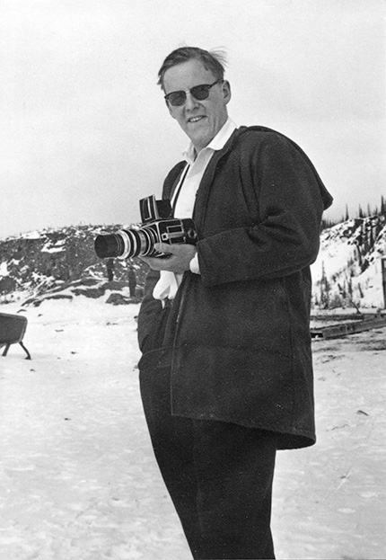 A black and white photo of a man standing outside while holding a camera.