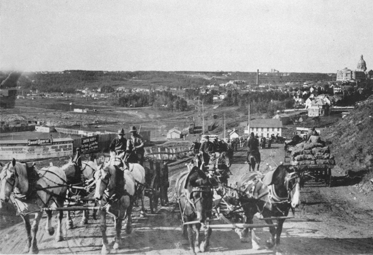 A black and white photo of horses pulling supplies on carriages.