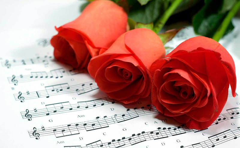 Three red roses sitting on a piece of sheet music.