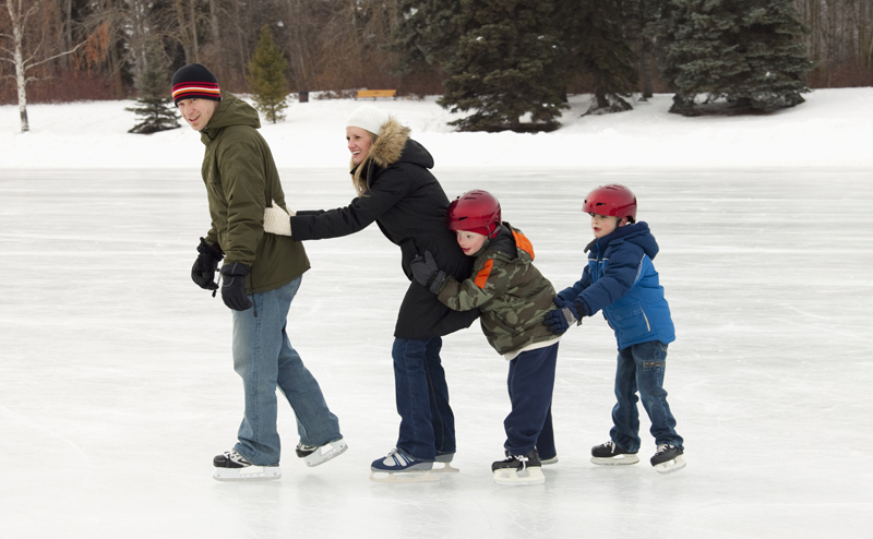 A family skating on outdoor ice. Each family member is holding the one in front of them, like a conga line.