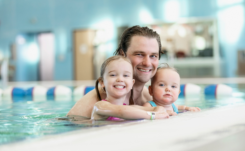 A man, a young girl, and a baby posing for a photo near the edge of a pool.