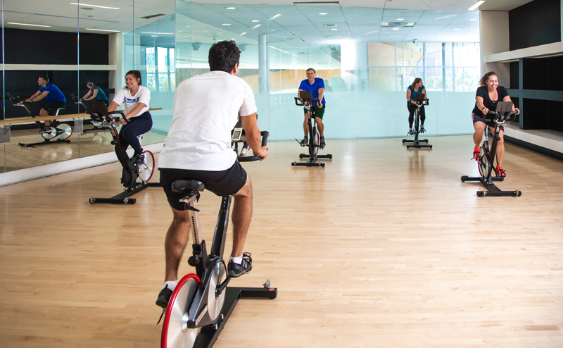 An instructor and four students riding stationary bikes in a studio space.