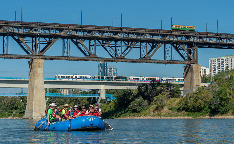 People in red life jackets using oars to paddle a blue inflatable boat.
