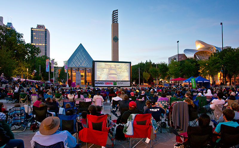 A crowd gathered in front of a screen at Churchill Square for Movies on the Square