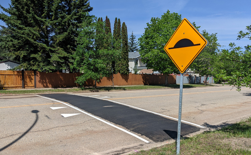 yellow traffic sign beside newly installed asphalt bump on road