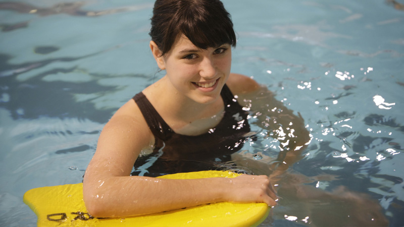 A woman in a pool, leaning on a flotation device.