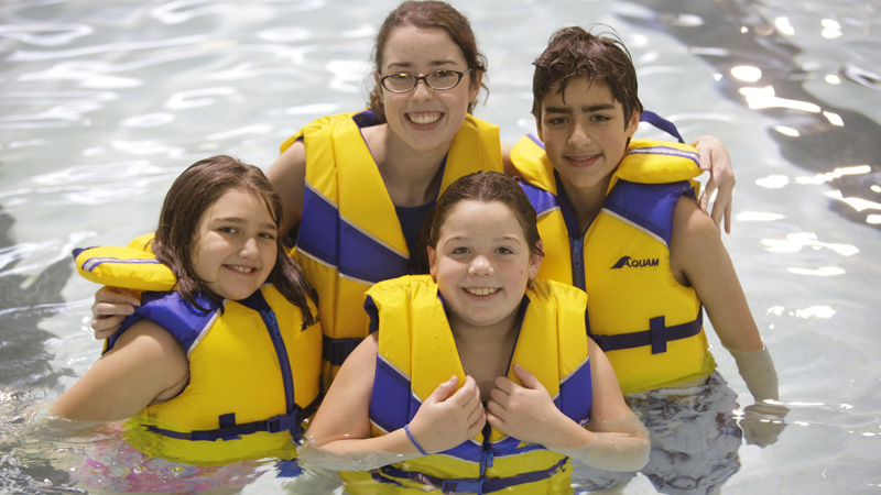 Four kids in life jackets posing for a photo in a pool.