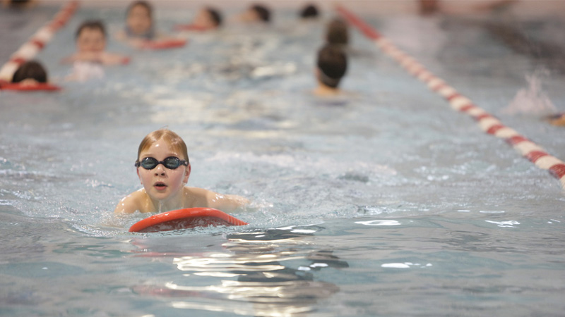 A kid in goggles lane swimming while holding a kick board.