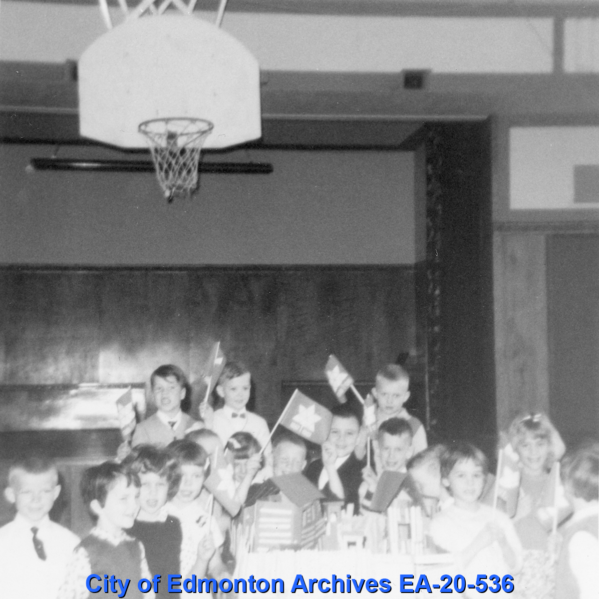 A black and white photograph of several children waving small flags with the official Centennial symbol.