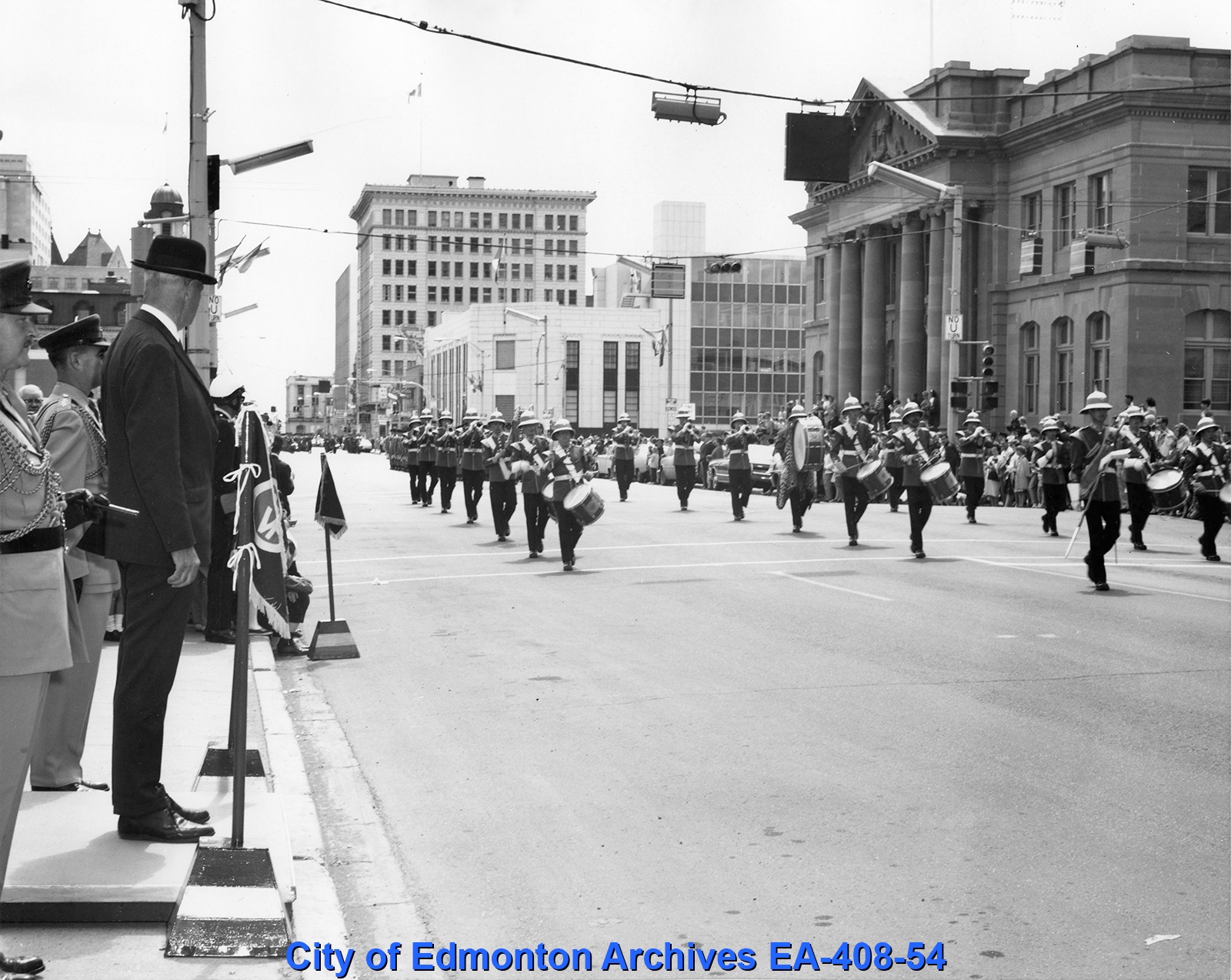 A black and white photograph of a marching band walking down a street.