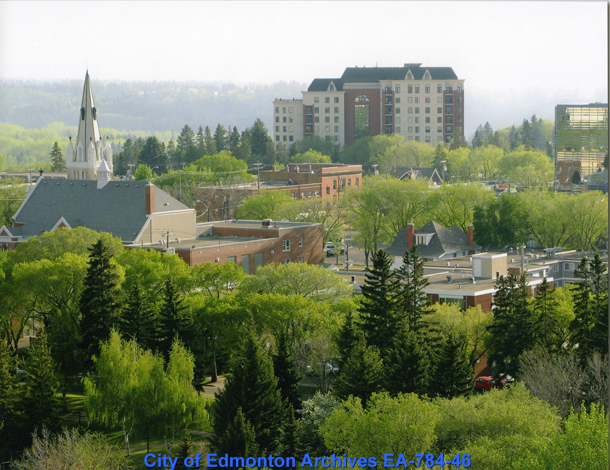The roof of a church and other buildings surrounded by vibrant green trees.