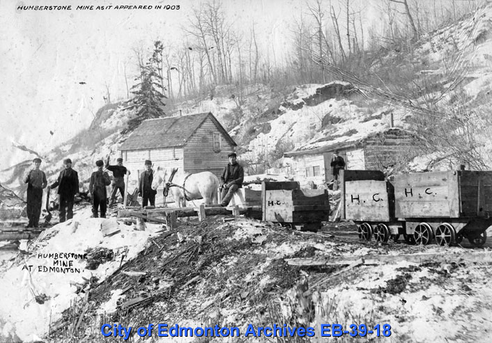 People and horses near a mine at the top of a hill.