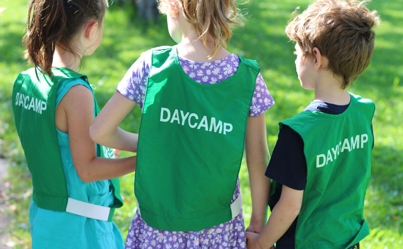 Three kids wearing green pinnies that say "Daycamp" on the back.