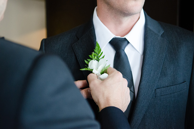 A man placing a boutonniere on another man's suit.