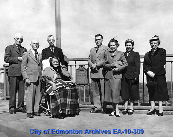 A group of people standing on a bridge, next to a plaque.
