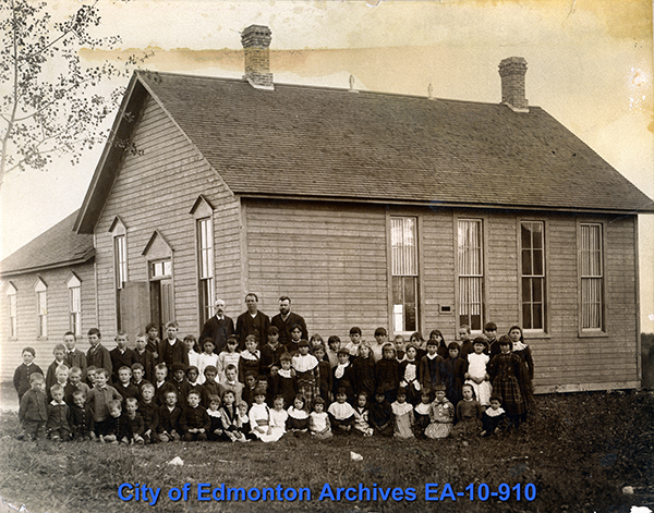 A school house with several students and teachers standing in front of it.