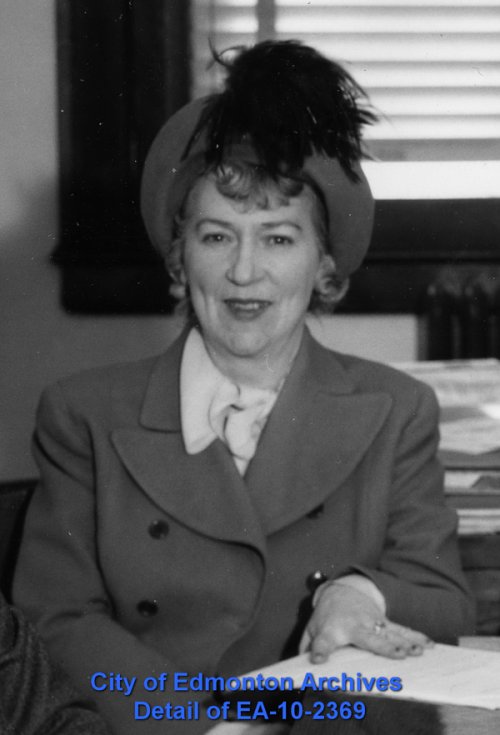A woman seated at a table, smiling towards the camera.