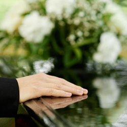 hand on top of casket with white rose
