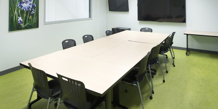 Four rectangular tables arranged to form a larger rectangular table. Ten rolling chairs surround the tables.