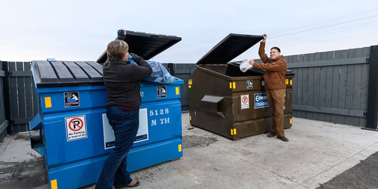 two persons standing beside recycle and garbage bins