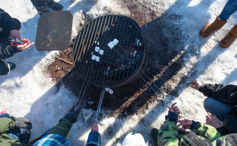 People roasting marshmallows over a grill in a park during winter.
