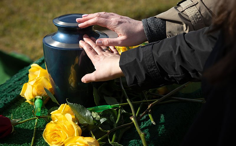 hands touching urn on top of burial stone