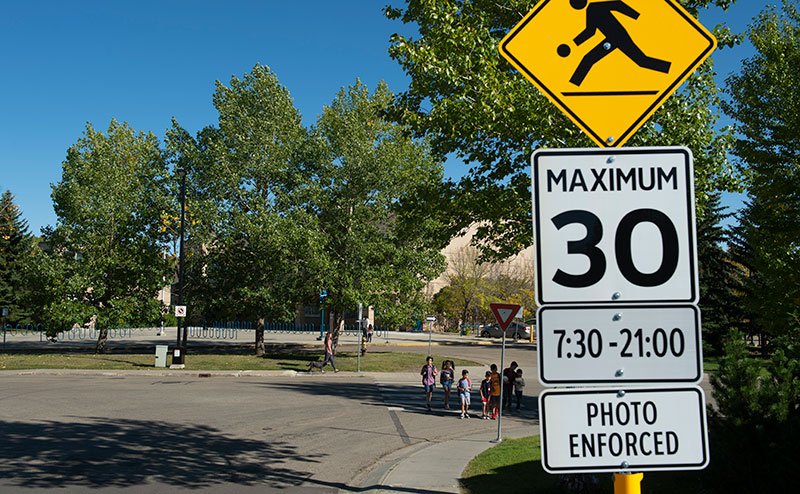 Playground zone speed limit sign with children crossing road in background