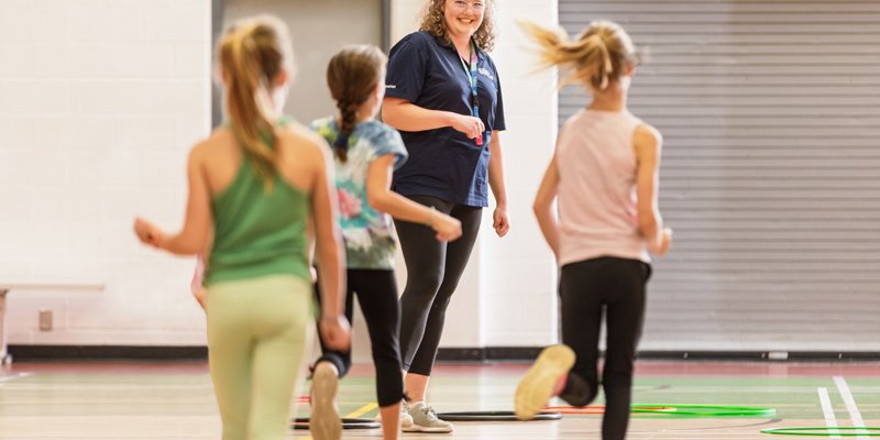 Three girls in a gymnasium, running toward an instructor.