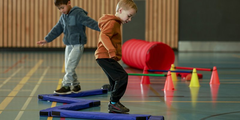 Two boys playing on a balancing beam mat in a gymnasium.