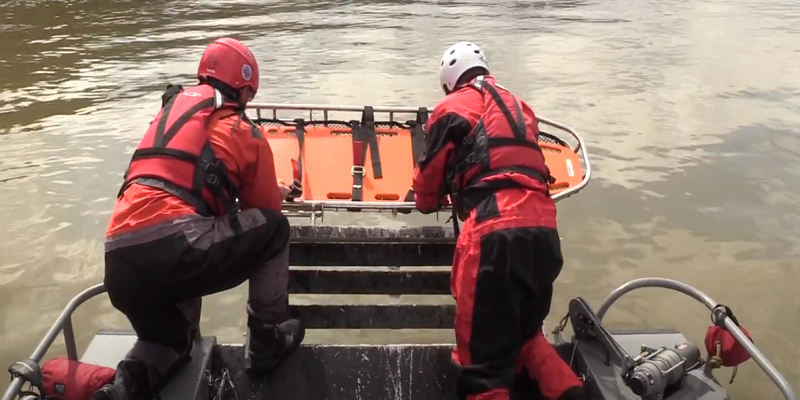 two men lowering stretcher into water