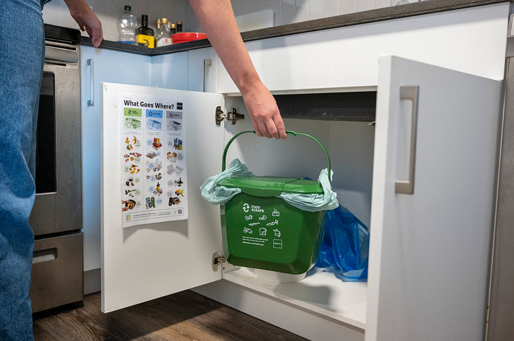 A person placing their food scraps pail in a kitchen cupboard.