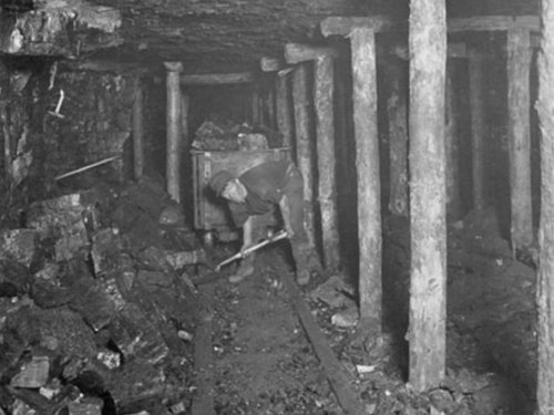 A mine worker next to a pile of coal and wooden pillars.