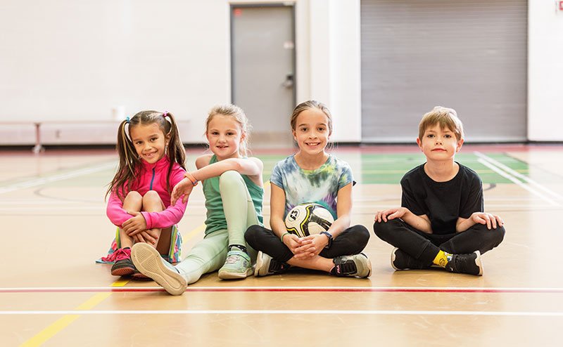 four kids sitting on gym floor