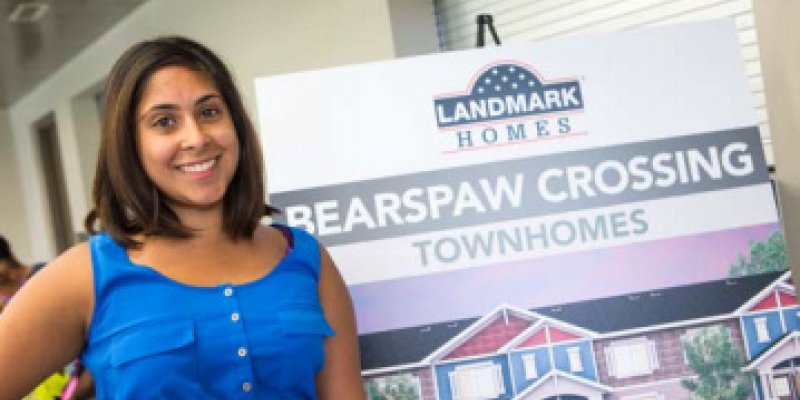 Alisha posing in front of a Bearspaw Crossing Townhomes poster